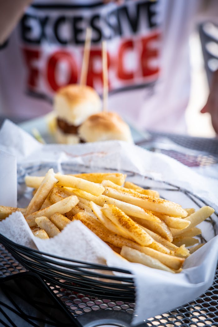 services-02 Tasty French fries with seasoning, served alongside mini burgers in a casual dining setting.